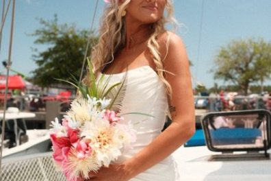 Bride in white dress holding pink flowers on a boat.